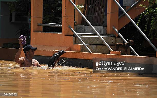 Local resident helps his pet, who fell into the water, to return to their home, partially covered by the water at a flooded street in the Tres Vendas...