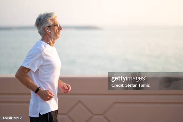 senior man running outside by the seaside at sunset - magro imagens e fotografias de stock