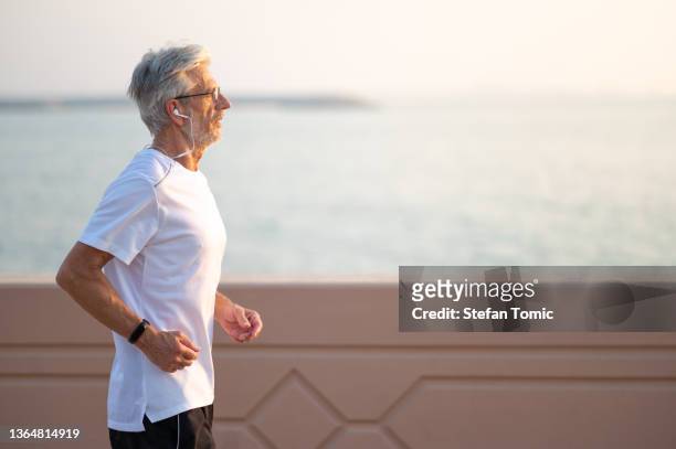 senior man running outside by the seaside at sunset - strong hair 個照片及圖片檔