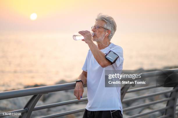 senior man drinking water during an exercise outside by the seaside at sunset - sea iphone stock pictures, royalty-free photos & images