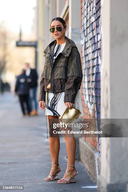 Tamara Kalinic wears aviator sunglasses, golden Fendi hair pins / brooch, golden long earrings, a golden necklace, a white short mini dress with...