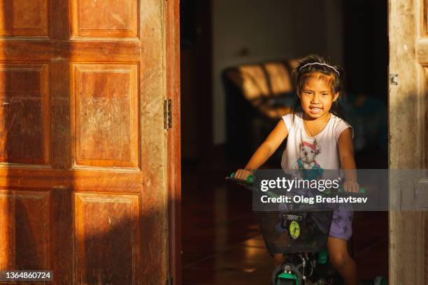 portrait of smiling asian girl on bicycle in house with beautiful sun light. childhood - very young thai girls stock pictures, royalty-free photos & images