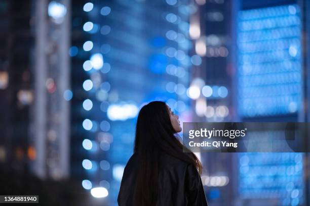 young asian woman using smartphone under skyscrapers in city - look stock-fotos und bilder
