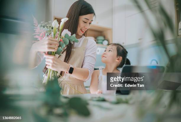 asiatische floristin, die sich mit der tochter verbindet, während sie in der küche am blumenarrangement arbeitet - chinese family taking photo at home stock-fotos und bilder