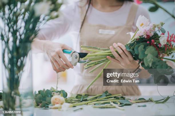 cerrar a la florista asiática china, dueña de una pequeña empresa cortando y arreglando el ramo de flores en la cocina de casa. rutina diaria de dirigir un trabajo de pequeña empresa desde casa - flower shop fotografías e imágenes de stock