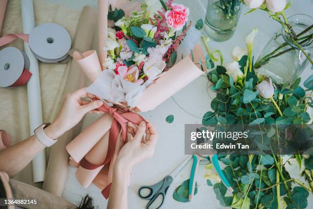 directamente encima de cerca de la floristería asiática china, propietaria de una pequeña empresa cwrapping flores ramo en la cocina de casa. rutina diaria de dirigir un trabajo de pequeña empresa desde casa - arreglo floral fotografías e imágenes de stock