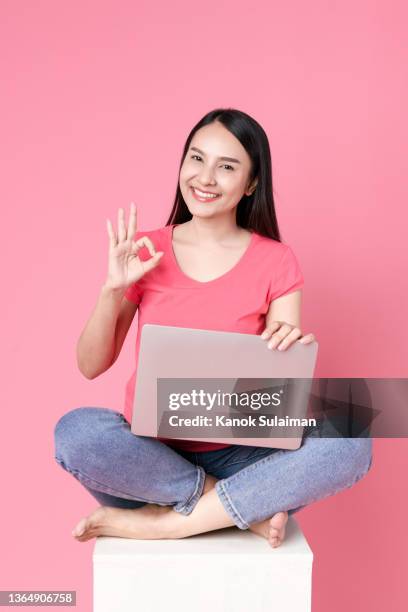 portrait of  happy woman gesturing over laptop while sitting on white box - okサイン　女性 ストックフォトと画像