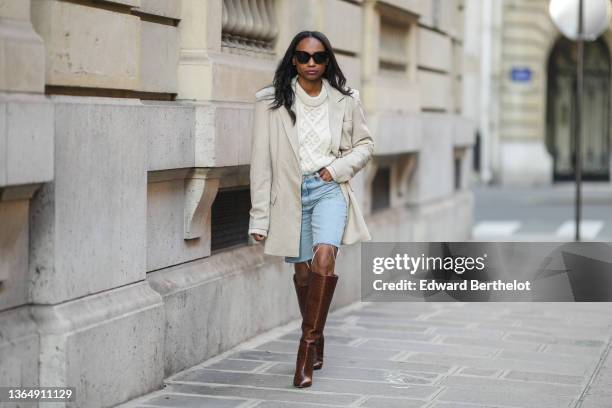 Emilie Joseph @in_fashionwetrust wears sunglasses, an oversized pinstripes beige blazer jacket by Sundarbay, a cable knit wool jumper pullover by...