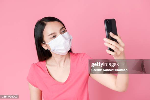 woman wearing mask taking selfie with mobile phone against pink background - man made object foto e immagini stock