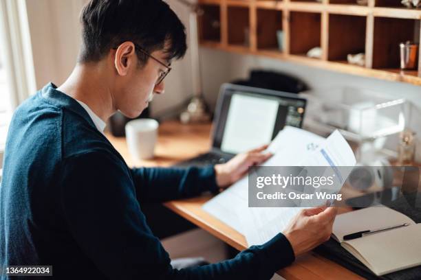 young asian man looking at financial bills while working on laptop at home - looking at bill home stock pictures, royalty-free photos & images