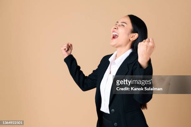 studio shot of cheering businesswoman with arms raised into fists celebrating good news - yes stockfoto's en -beelden