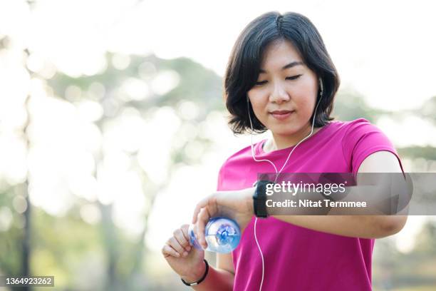 heart rate variability trends. asian female drinking water and checking heart rate on smartwatch after jogging on trails in public park. - normal ecg results foto e immagini stock