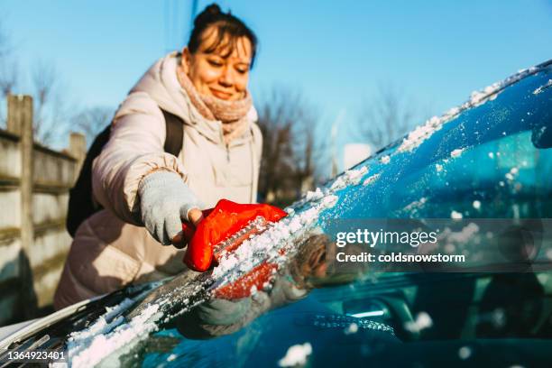 woman scraping ice from car on winter morning - voorruit stockfoto's en -beelden