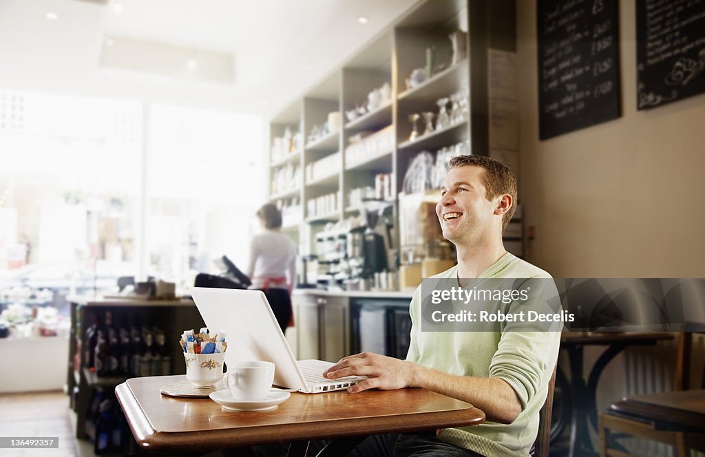 Man using lap top in cafe laughing