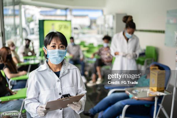 portrait of doctor holding a clipboard on a vaccination center - entering hospital stock pictures, royalty-free photos & images