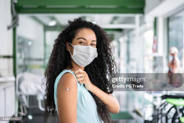 portrait of a young woman showing her arm after vaccination - vaccine confidence stock pictures, royalty-free photos & images