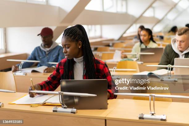 young afro-american student is writing in the library - school exam stockfoto's en -beelden