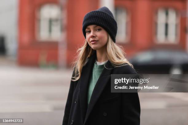 Isabelle Hartmann wearing green Anine Bing sweater, black vintage coat, and black Acne Studios beanie on January 14, 2022 in Hamburg, Germany.