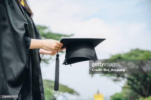 student wearing graduation gown and holding a graduation cap. - graduates stockfoto's en -beelden