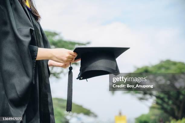 student wearing graduation gown and holding a graduation cap. - graduates stock pictures, royalty-free photos & images