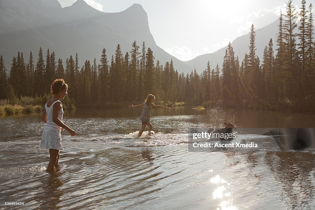 Two young girls play in a mountain pond with a dog