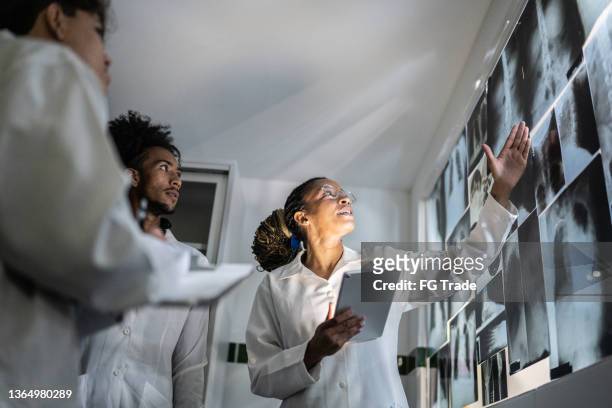 teacher holding a digital tablet and explaining about xrays to students - black lab stockfoto's en -beelden