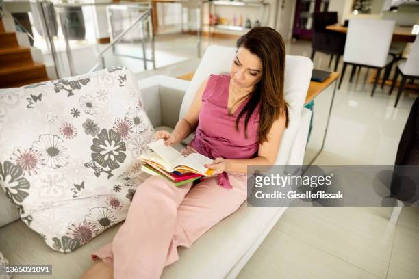 giovane donna che legge un libro a casa - sfogliare libro foto e immagini stock