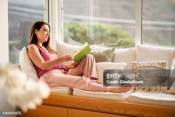 bella giovane donna che legge un libro a casa - sfogliare libro foto e immagini stock