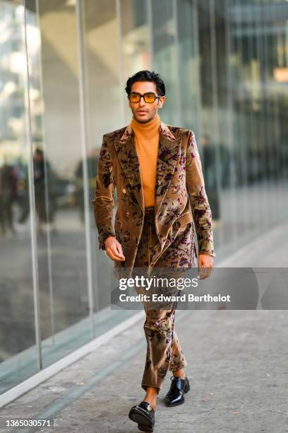 Rahi Chadda wears orange/brown transparent sunglasses, an orange turtleneck pullover, a brown oversized velvet blazer jacket with floral print,...