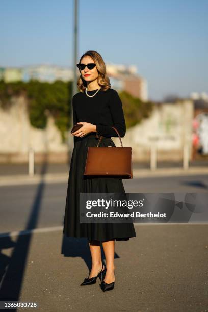 Jenny Walton wears sunglasses, a pearl beaded necklace, a black pullover, a brown rectangular briefcase shaped leather bag from Celine, a black...