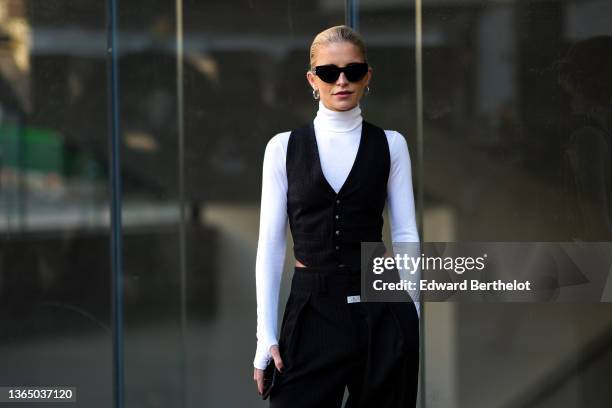 Caroline Daur wears sunglasses, earrings, a white turtleneck top, a sleeveless jacket from a three-piece suit, matching striped black suit pants,...