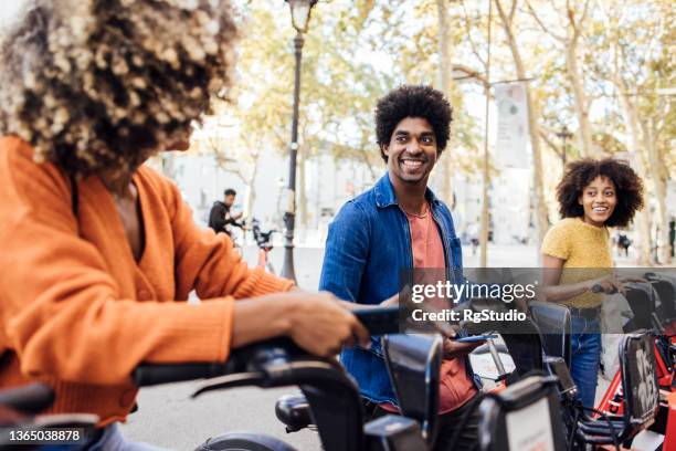 three afro friends having fun in barcelona, renting e-bikes - bike sharing stock pictures, royalty-free photos & images