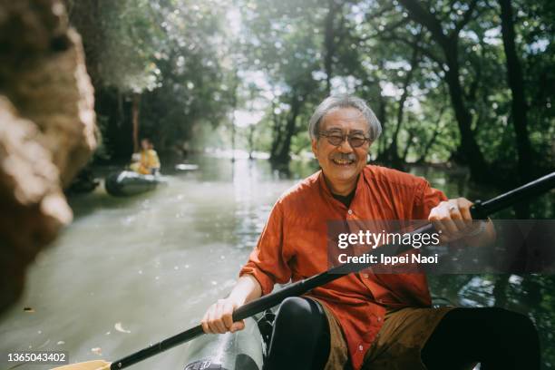 senior man enjoying kayaking through jungle river - okinawa prefecture stock-fotos und bilder