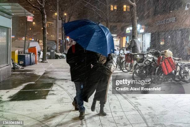 People walk through the snow holding an umbrella against the wind and snow caused by Winter Storm Izzy on January 16, 2022 in New York City. Despite...