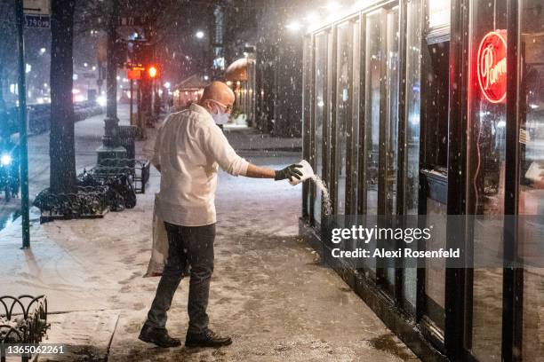 Restaurant worker salts the ground outside a restaurant in the snow during Winter Storm Izzy on January 16, 2022 in New York City. New York City...