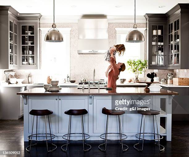 mother lifting daughter in kitchen - kitchen stock-fotos und bilder