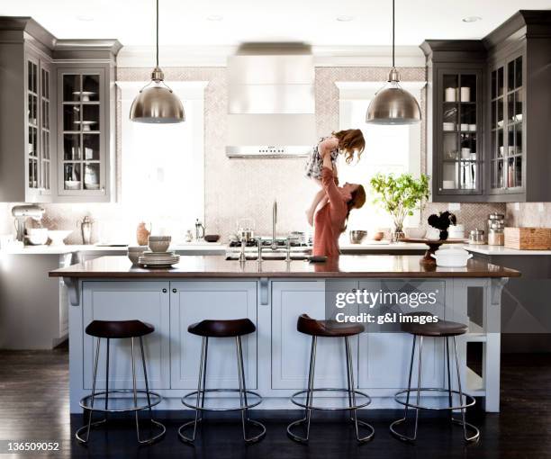 mother lifting daughter in kitchen - at home 個照片及圖片檔