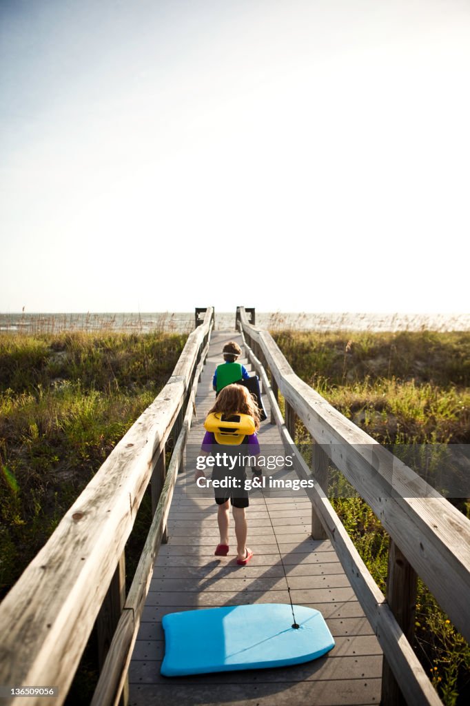 2 children walking down boardwalk with boogie boar