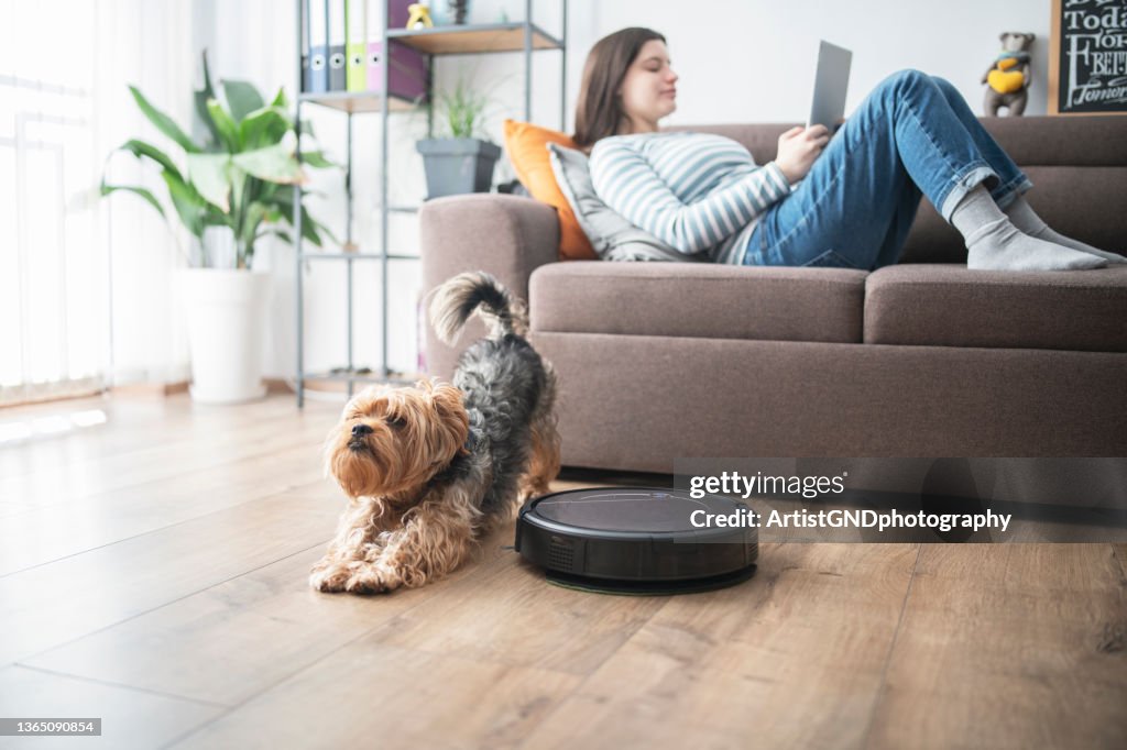 Woman and dog relaxing in the living room while robot vaccum cleans.