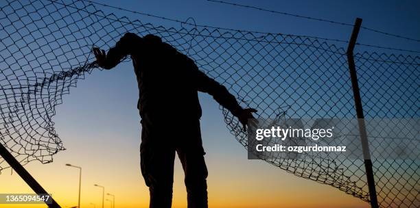 refugee man running behind fence - refugee silhouette stock pictures, royalty-free photos & images