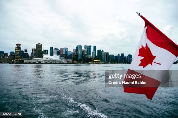 canadian flag flying over river and vancouver city skyline, viewed from boat on an overcast day - vancouver skyline stock-fotos und bilder