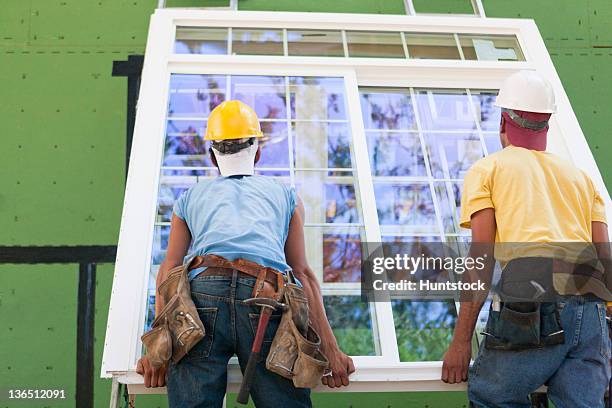 carpenters positioning a large window frame at a construction site - objects fitting together stock pictures, royalty-free photos & images