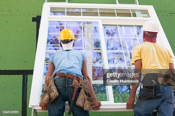 carpenters positioning a large window frame at a construction site - window installation stock pictures, royalty-free photos & images