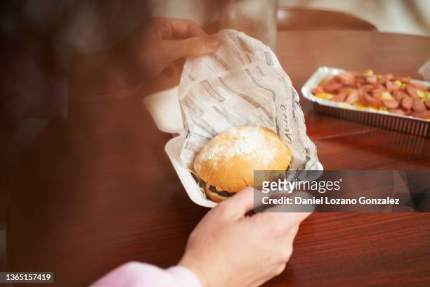crop female unwrapping burger on dining table - fastfood restaurant table stock-fotos und bilder