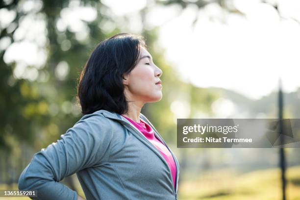 rest and recovery after exercise.  side view of asian working women take a rest after outdoors workout in a city park. - respirar imagens e fotografias de stock