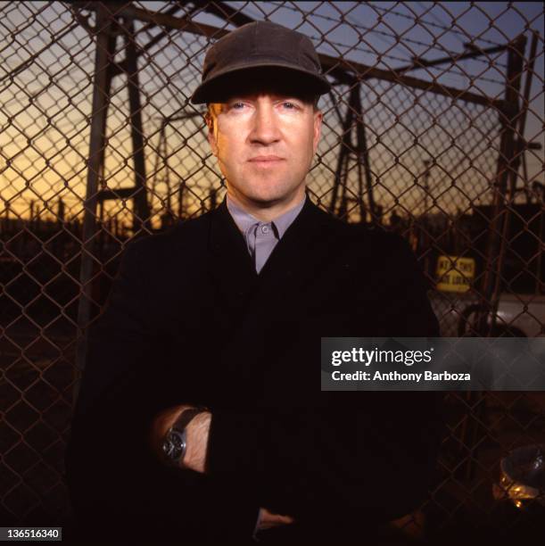 Portrait of American film and television director David Lynch as he poses in front of a chain-link fence, Los Angeles, California, 1989.