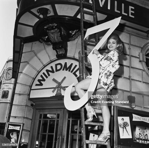 Marilyn Maxwell carrying an outsize number 3 in front of the Windmill Theatre in Soho, London, UK, 4th February 1964.