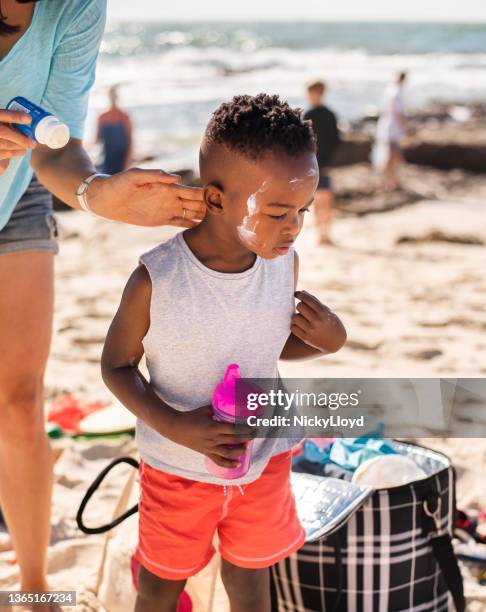 mom putting suntan lotion on her little son's face at the beach - putting lotion stock pictures, royalty-free photos & images