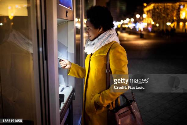 夜にatmでクレジットカードで取引をする若いアフリカ系アメリカ人女性 - bank statement ストックフォトと画像