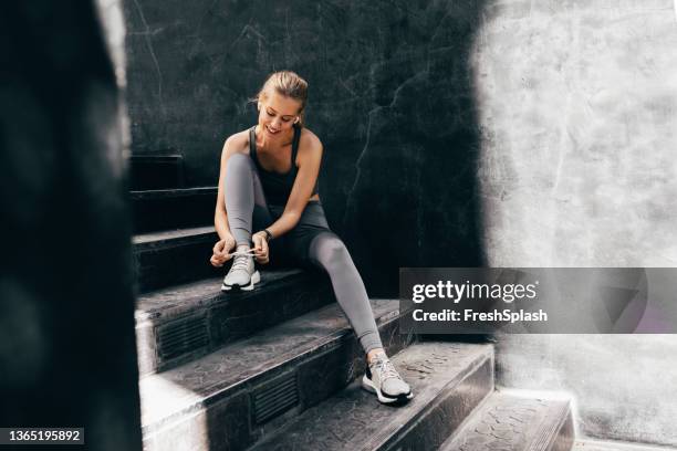 pronto per un allenamento all'aperto: felice donna bionda legare i lacci su scarpe da ginnastica - calzature sportive foto e immagini stock